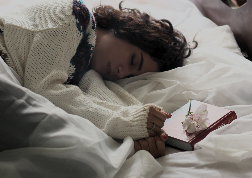 Woman with sweater sleeping soundly - White sheets - Book - White flower