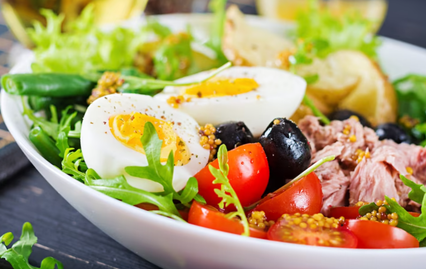 Healthy hearty salad of tuna, green beans, tomatoes, eggs, potatoes, black olives close-up in a bowl on the table
